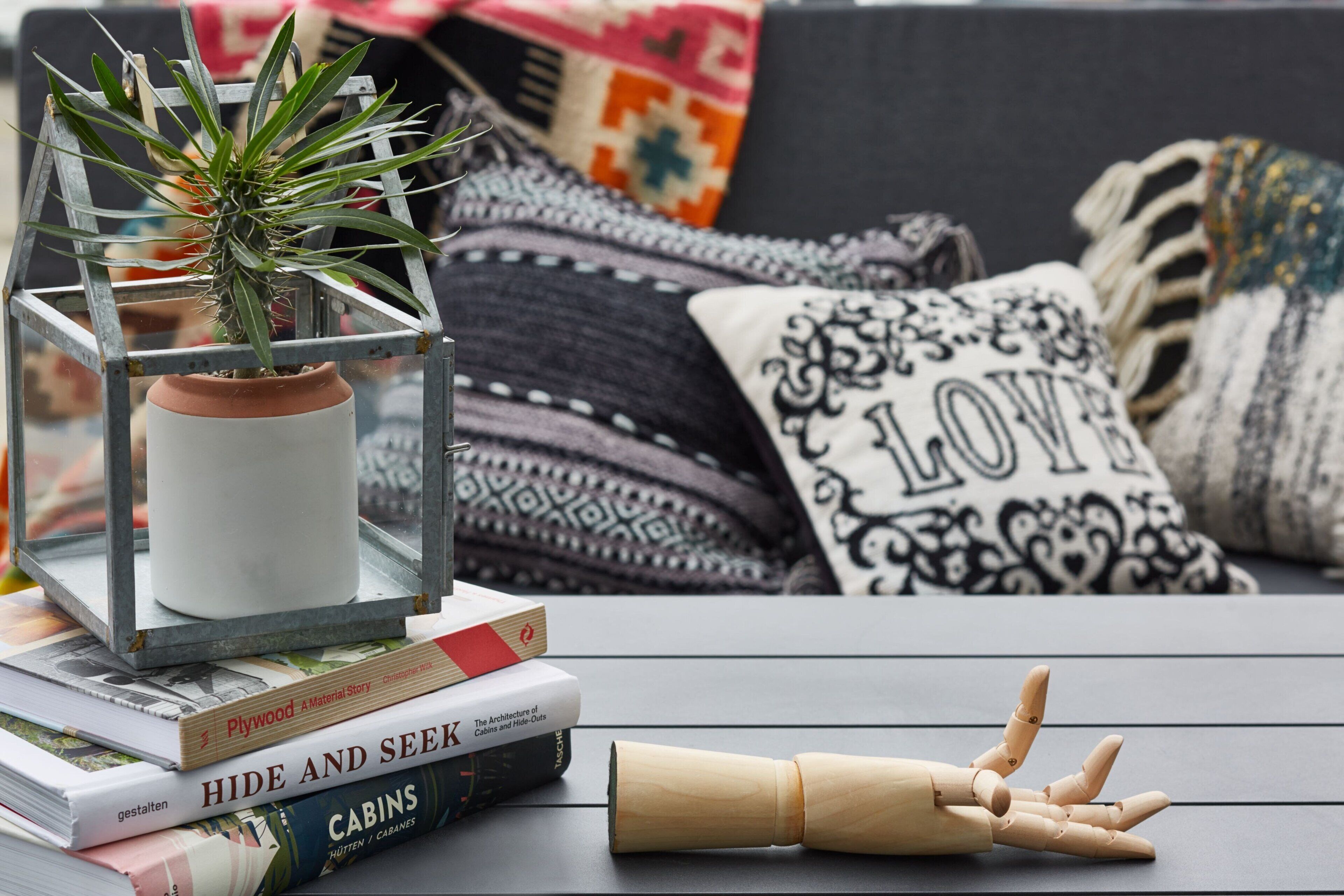 A cozy reading nook with a clear glass terrarium containing a plant, a stack of books, and a wooden mannequin.