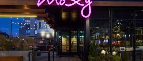 Un edificio moderno con un letrero de neón que dice "moxy" y una entrada de vidrio.