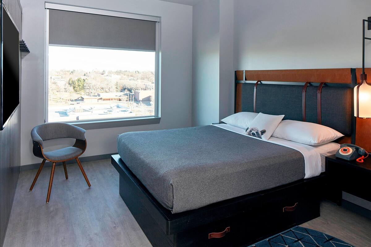 Een moderne hotelkamer met een groot bed, een stoel, een nachtkastje met een lamp en een raam met uitzicht op gebouwen.