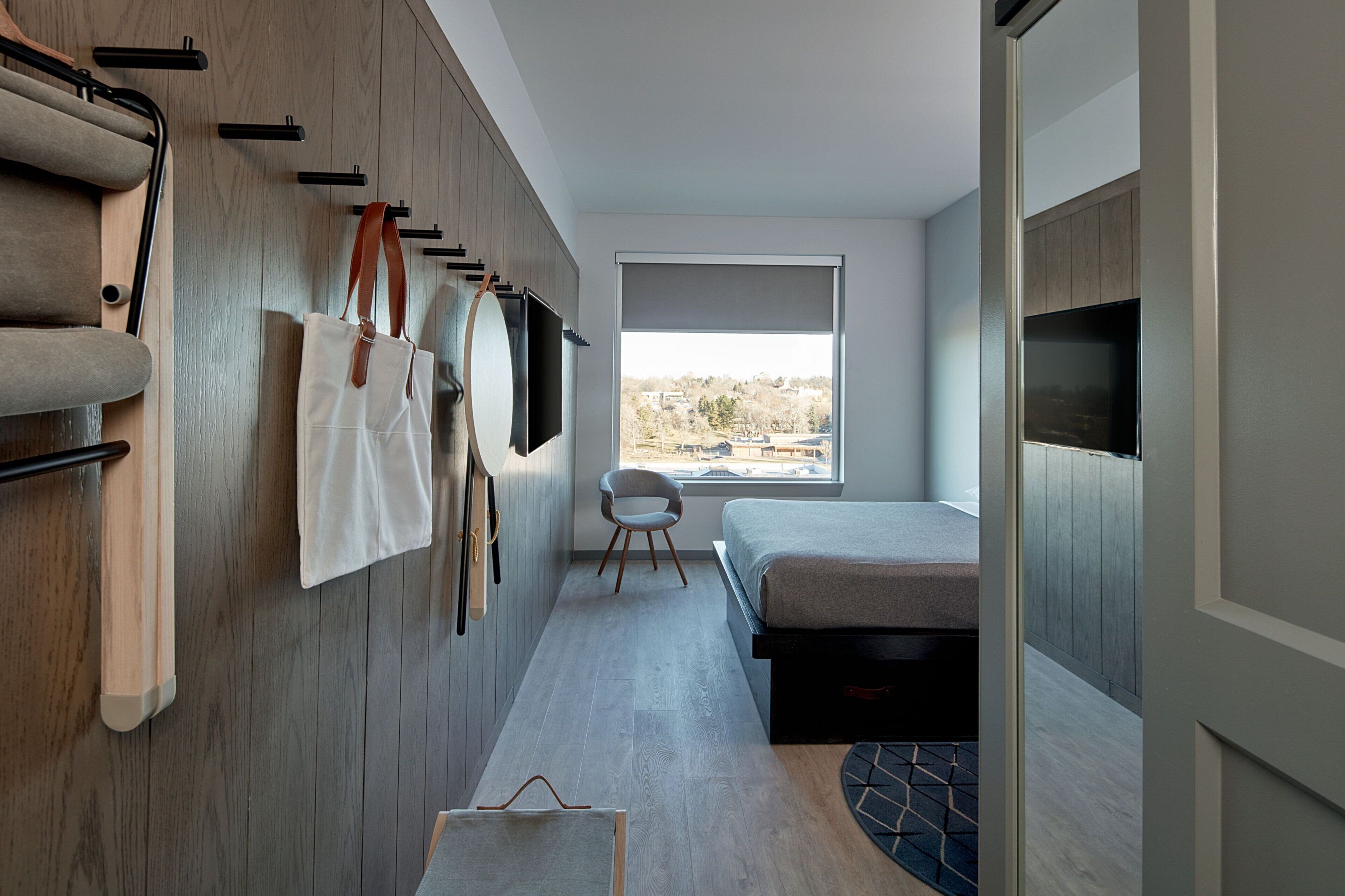 Una habitación de hotel moderna con cama, una silla, televisor y ventana con vistas.