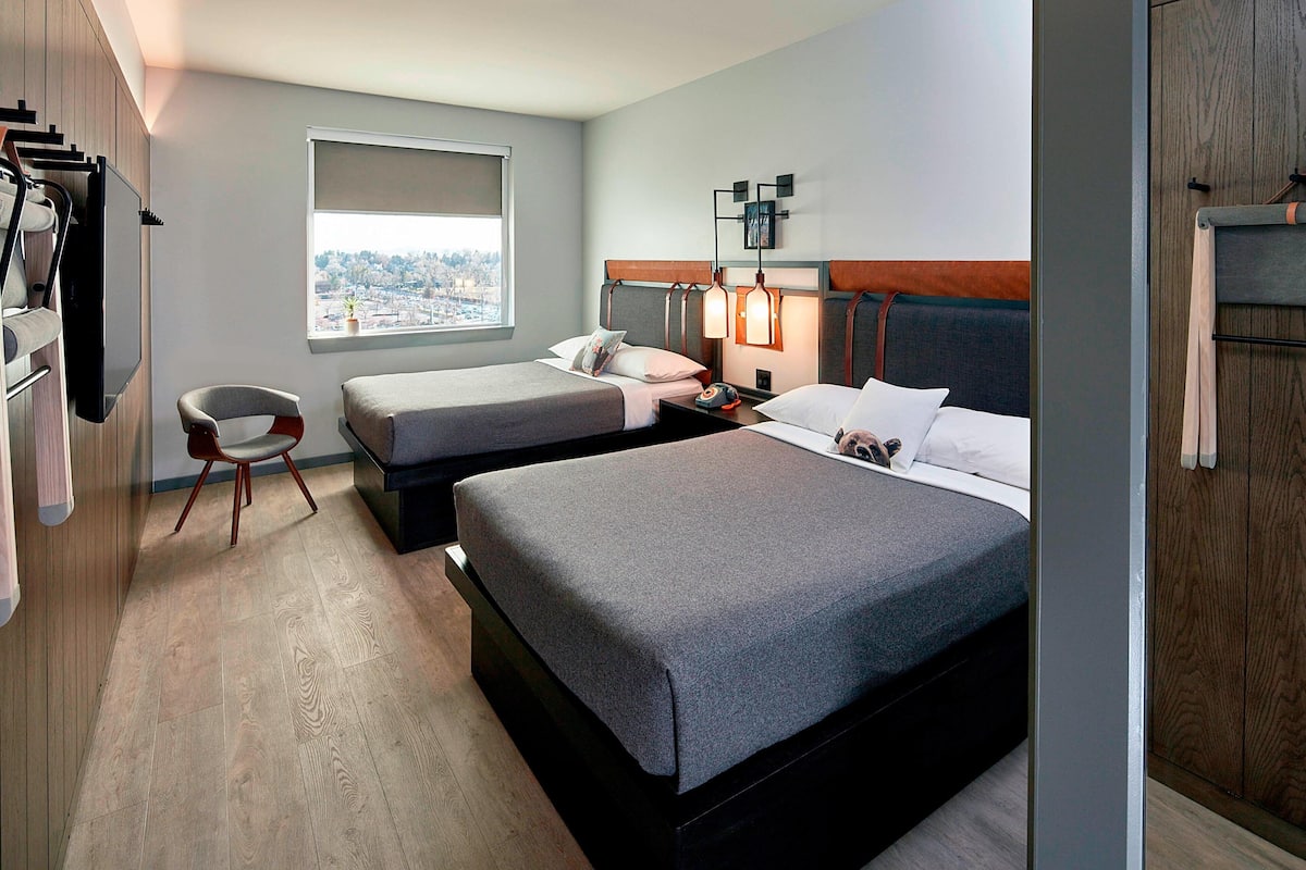Hotelkamer met twee bedden, een bureau, een stoel, een televisie en een raam met uitzicht over de stad.