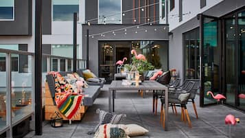 Un área de estar al aire libre con un sofá, sillas y una mesa, decorada con flamencos y luces colgantes.