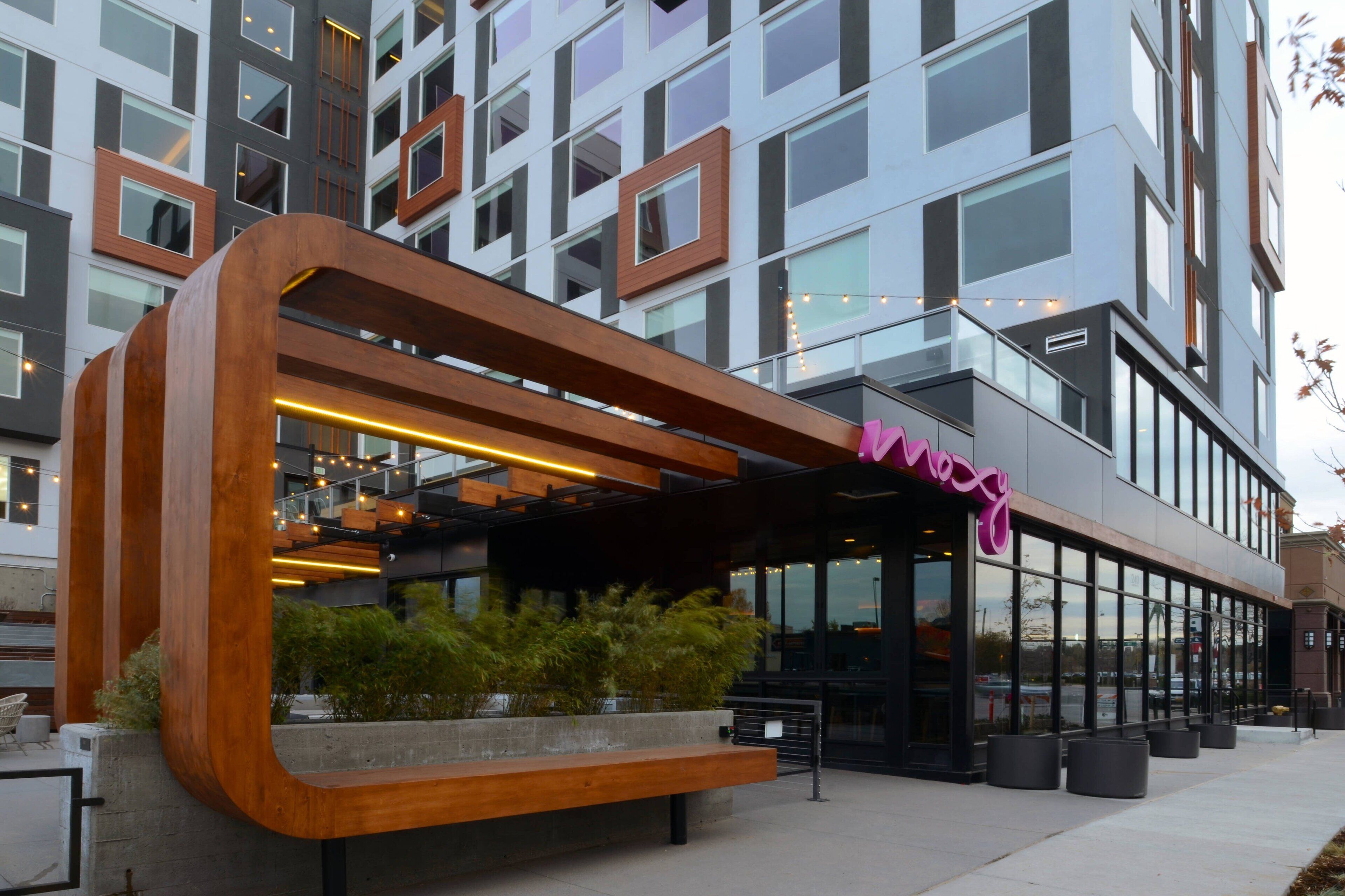 A modern building with a large wooden structure in front, a glass facade, and a sign that reads "Mossy."