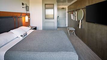 A hotel room with a large bed, a bedside table with a lamp, a wall-mounted TV, and a door leading to a bathroom.