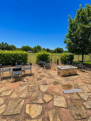 An outdoor patio with stone flooring, metal chairs, a fire pit, and a green fence. - Courtyard by Marriott Austin Northwest/Lakeline (Austin)