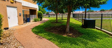 A pathway leading to a building with a garage, a fenced area, and a tree-lined lawn.
