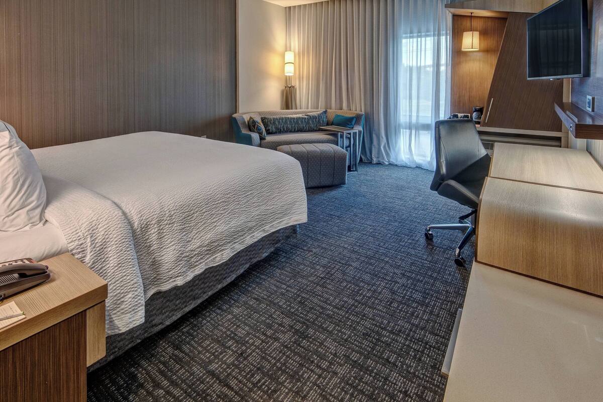 Ein Hotelzimmer mit einem großen Bett, einem Schreibtisch mit Telefon, einem Sessel, einer Couch und einem Fernseher.