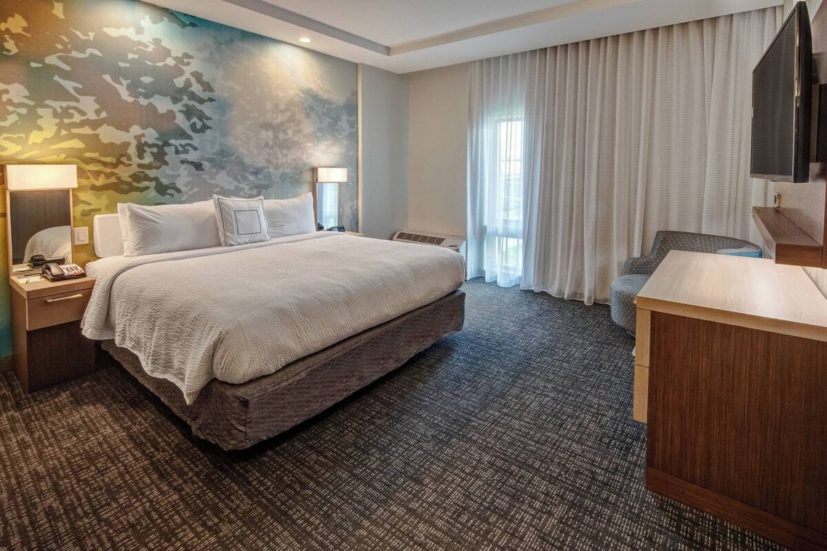 Ein Hotelzimmer mit einem großen Bett, einem Schreibtisch, einem Sessel, einem Fernseher und einer Wand mit einem Tarnmuster.