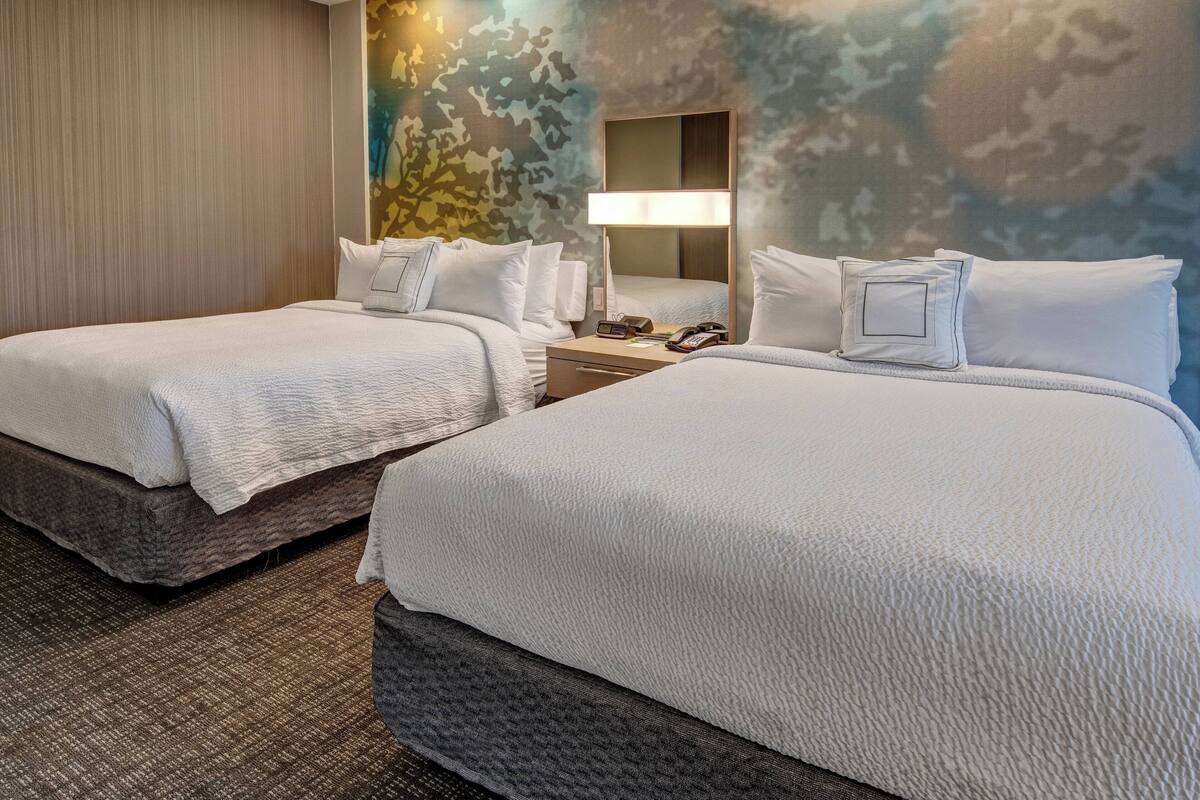 Ein Hotelzimmer mit zwei Betten, einem Nachttisch, einer Lampe und einer Wand mit einem Tarnmuster.