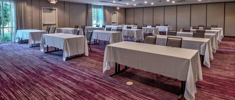 A conference room with multiple tables and chairs, carpeted flooring, and large windows.