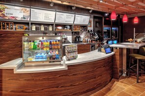 A bistro counter with a refrigerated display of beverages, a menu board above, and a bar area with red pendant lights. - Courtyard by Marriott Austin Northwest/Lakeline (Austin)