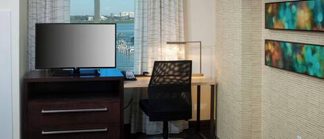 Habitación de hotel con escritorio, televisión y una obra de arte en la pared.