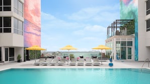 Un espace piscine intérieur moderne, doté de chaises longues et de parasols jaunes, entouré de murs de verre et offrant une vue sur la ville.