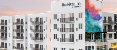 A modern multi-story hotel with balconies, a rooftop terrace, and a colorful mural.