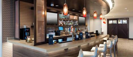 A modern bar area with a curved counter, multiple hanging pendant lights, and bar stools.