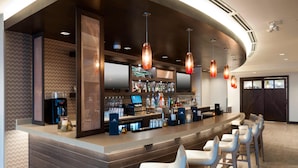 Un área de bar moderna con una barra curva, múltiples luces colgantes y taburetes.