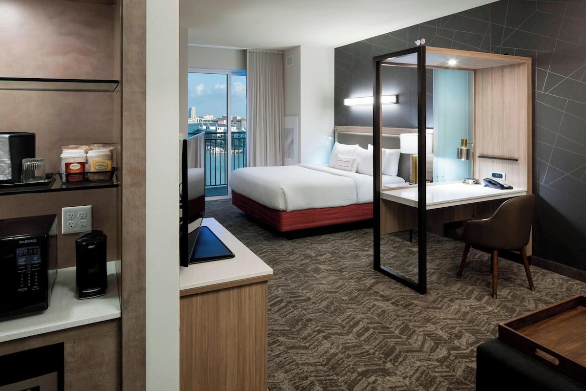 Ein Hotelzimmer mit Bett, Schreibtisch, Stuhl, Minibar und Blick auf die Stadt.