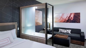 Una habitación de hotel moderna con una cama grande, un sofá, una mesita y un separador de vidrio.