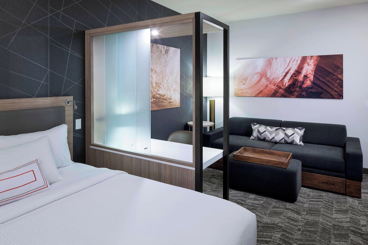 Ein modernes Hotelzimmer mit einem großen Bett, einer Couch, einem kleinen Tisch und einer Glastrennwand.