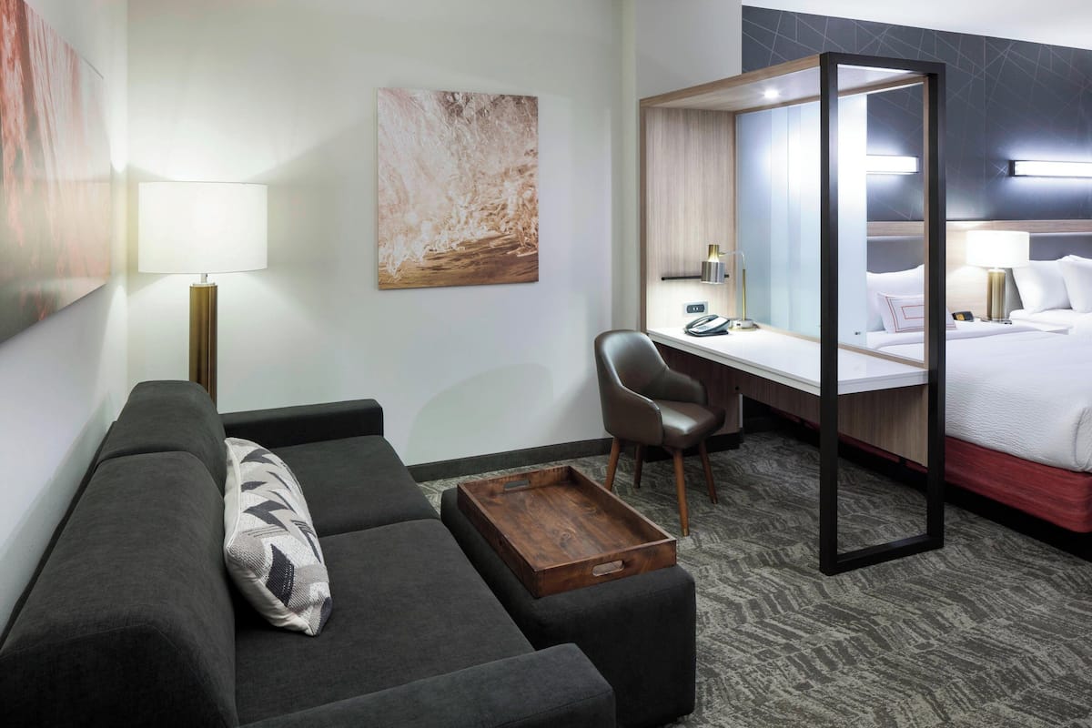 Ein modernes Hotelzimmer mit einer Sitzecke, einem Schreibtisch, einem Bett und einem großen Spiegel.
