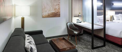Une chambre d’hôtel moderne équipée d’un canapé, d’un bureau, d’un lit et d’un grand miroir.