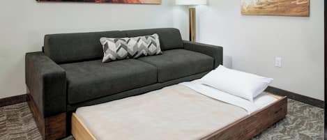 Een moderne hotelkamer met een grijze bank, een houten bedframe en twee abstracte schilderijen aan de wand.