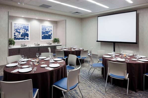 A conference room with round tables, chairs, and a projector screen.
