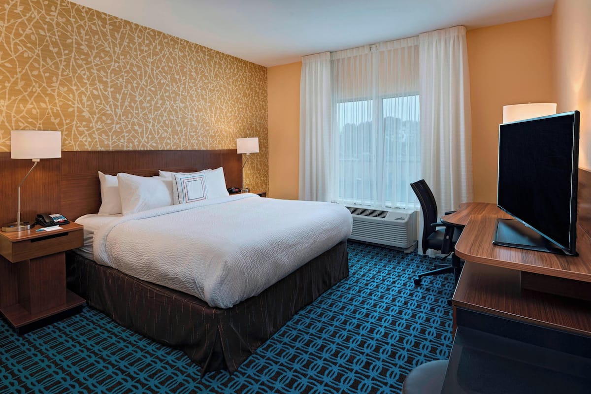 Une chambre d’hôtel avec un grand lit, deux tables de chevet avec des lampes, un bureau avec un téléviseur à écran plat et une moquette à motifs.