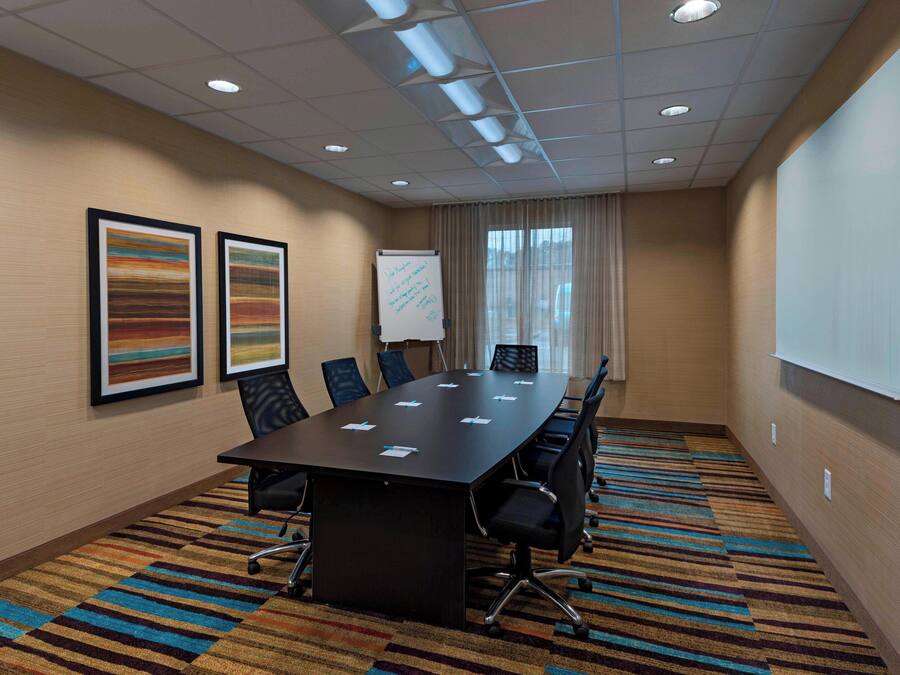 A conference room with a long table, chairs, a whiteboard, and two framed artworks on the wall.