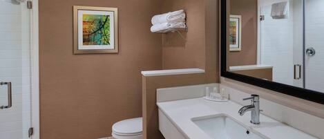 Un baño moderno con inodoro, lavamanos y ducha. Hay un cuadro en la pared y un perchero con toallas.