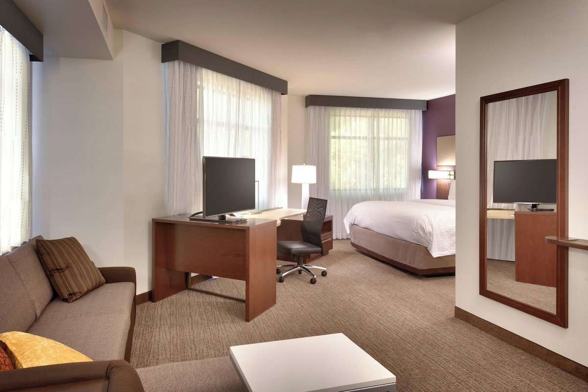A hotel room with a bed, a desk with a computer, a chair, a sofa, and a TV.