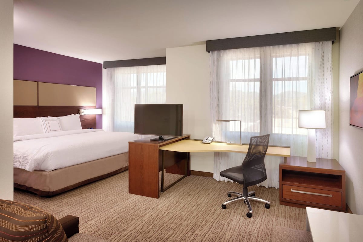 A hotel room with a bed, a desk with a computer, a chair, and a TV.