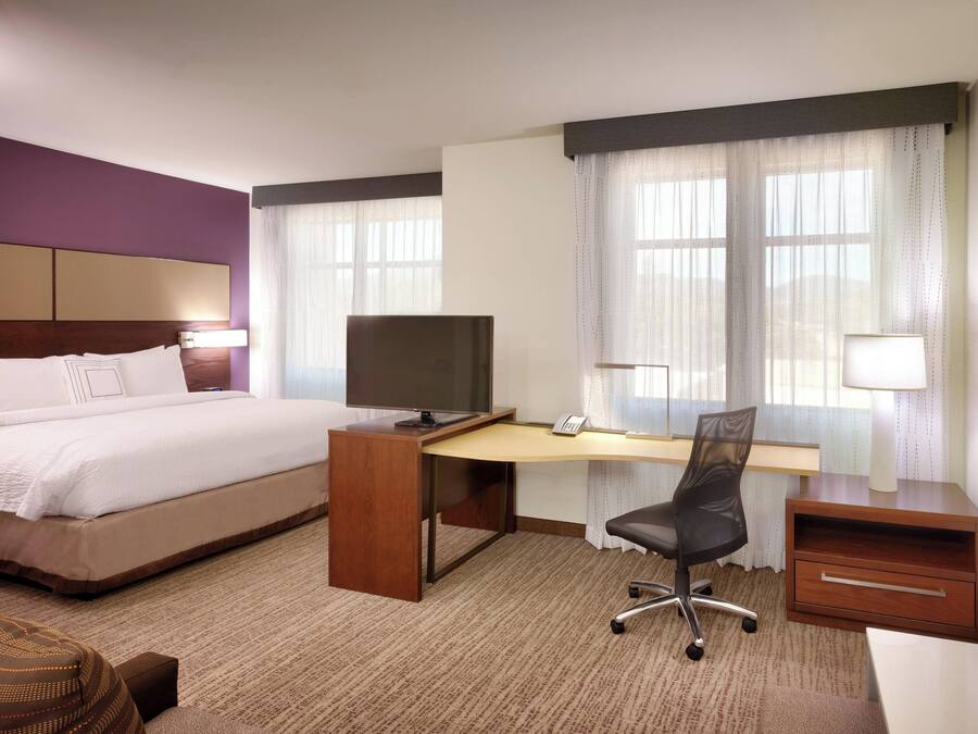 A hotel room with a bed, a desk with a computer, a chair, and a TV.
