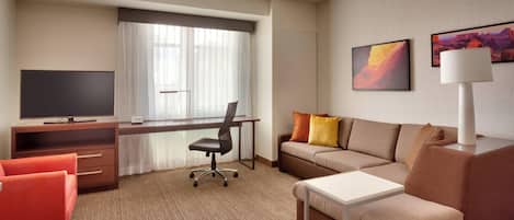 A hotel room with a large window, a flat-screen TV, a desk, a sofa, and a lamp.