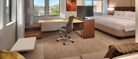 A hotel room with a bed, desk, chair, and large windows.