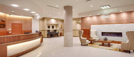 A modern hotel lobby with a reception desk, seating area, and a fireplace.