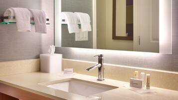 A modern bathroom with a large mirror, a sink with a chrome faucet, and two towels hanging on a towel rack.