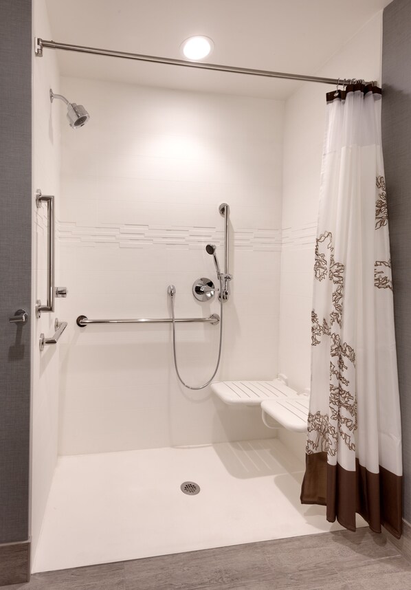A walk-in shower with a glass door, a showerhead, a handheld shower, and a shower curtain.