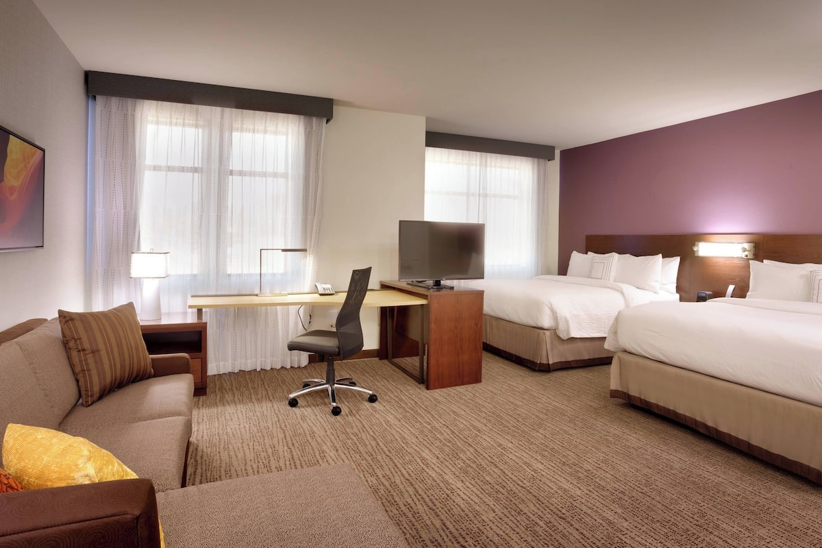 A hotel room with a bed, a desk with a chair, a sofa, and a TV.