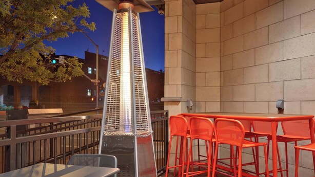 An outdoor seating area with a tall, metallic heater, orange chairs, and a stone wall. - Residence Inn by Marriott Flagstaff (Flagstaff)