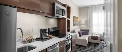 A modern kitchen with a built-in microwave, stainless steel appliances, and a coffee maker. There is a seating area with a sofa and a small table.