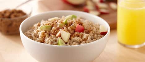 A bowl of oatmeal with diced apples and a glass of orange juice on a wooden table.