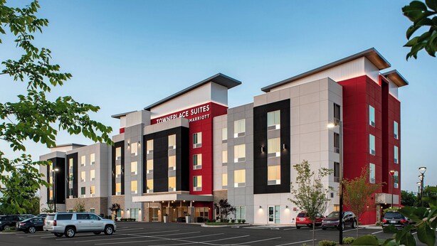 A modern hotel with a red and white facade, multiple floors, and a parking lot with several cars. - TownePlace Suites by Marriott Charlotte Fort Mill (Fort Mill)