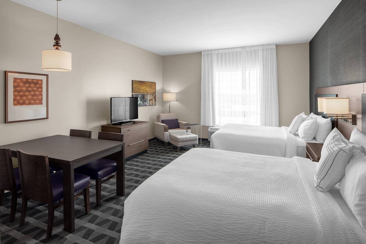 Habitación de hotel con una cama grande, un escritorio con silla, televisión y ventana con cortinas.