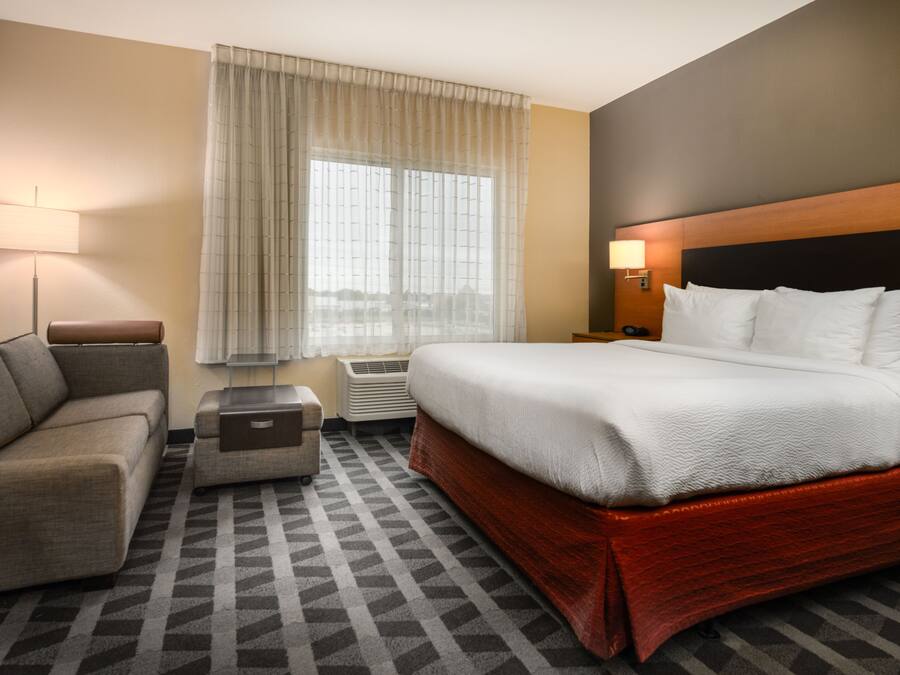 Una habitación de hotel con una cama, un sofá, una mesita y una ventana con cortinas.
