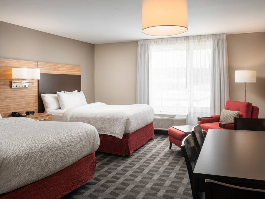 Ett hotellrum med två sängar, ett matbord, en röd fåtölj och ett stort fönster med tunna, genomskinliga gardiner.