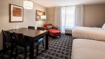 Hotelkamer met een eettafel, twee stoelen, een rode fauteuil, een lamp, een bed en een groot raam met gordijnen.