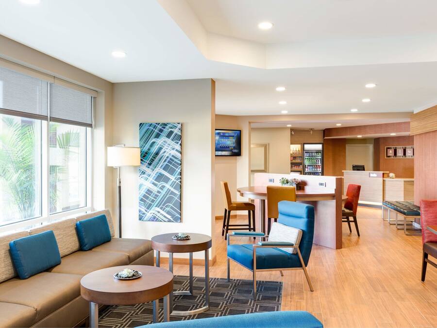 A hotel lobby with a sofa, chairs, a small table, a reception desk, and a TV screen.
