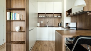 A compact kitchen with wooden shelves, a white countertop, and a black chair. - Apollis Business & Budget by Ambiente (Bratislava)