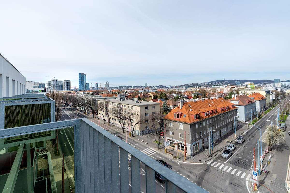 A cityscape with modern buildings, a wide street, and a pedestrian crossing.